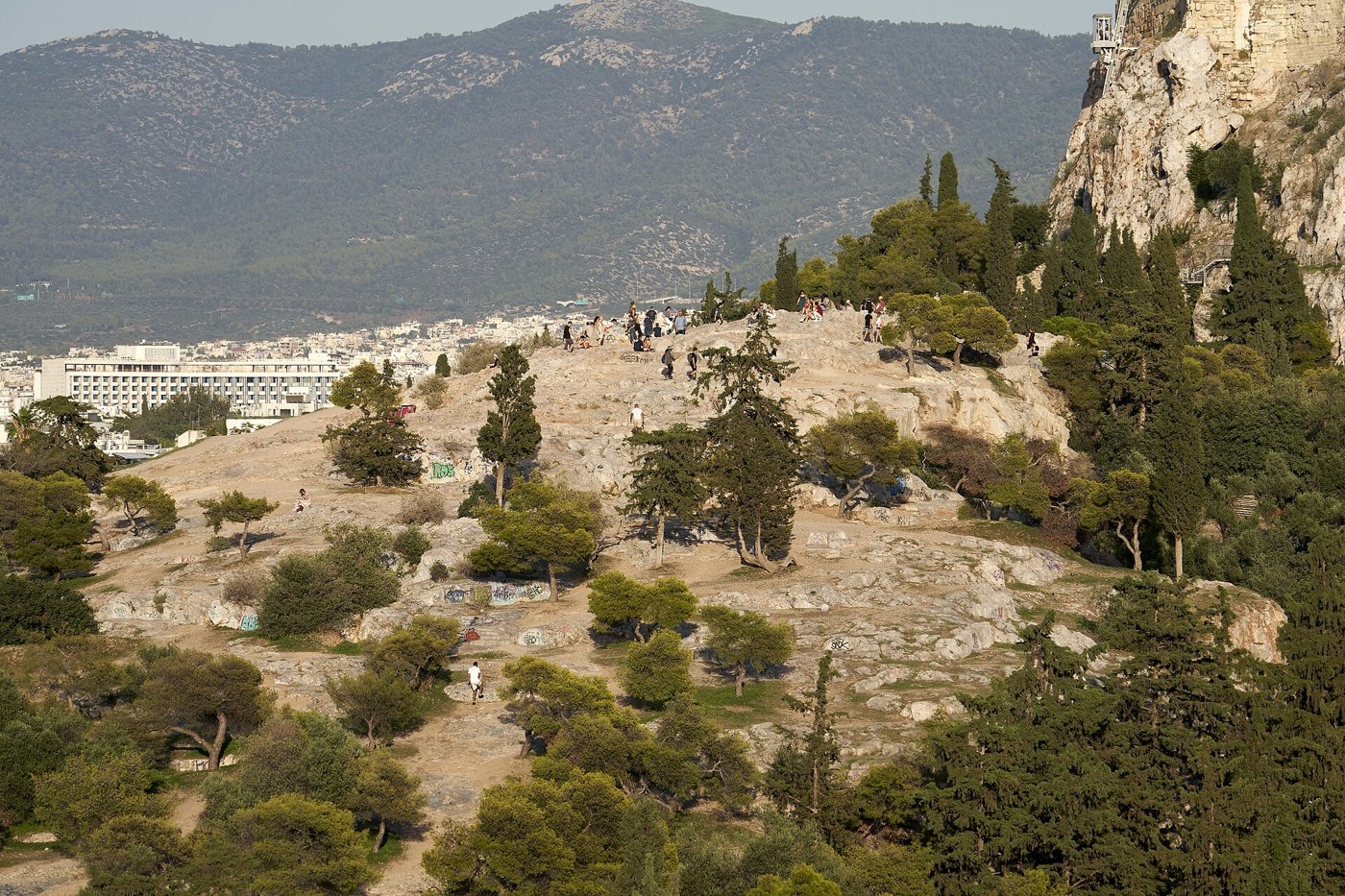 The bare limestone Areopagus (Mars Hill) with visitors on its summit, seen from the Pnyx below the Acropolis cliff