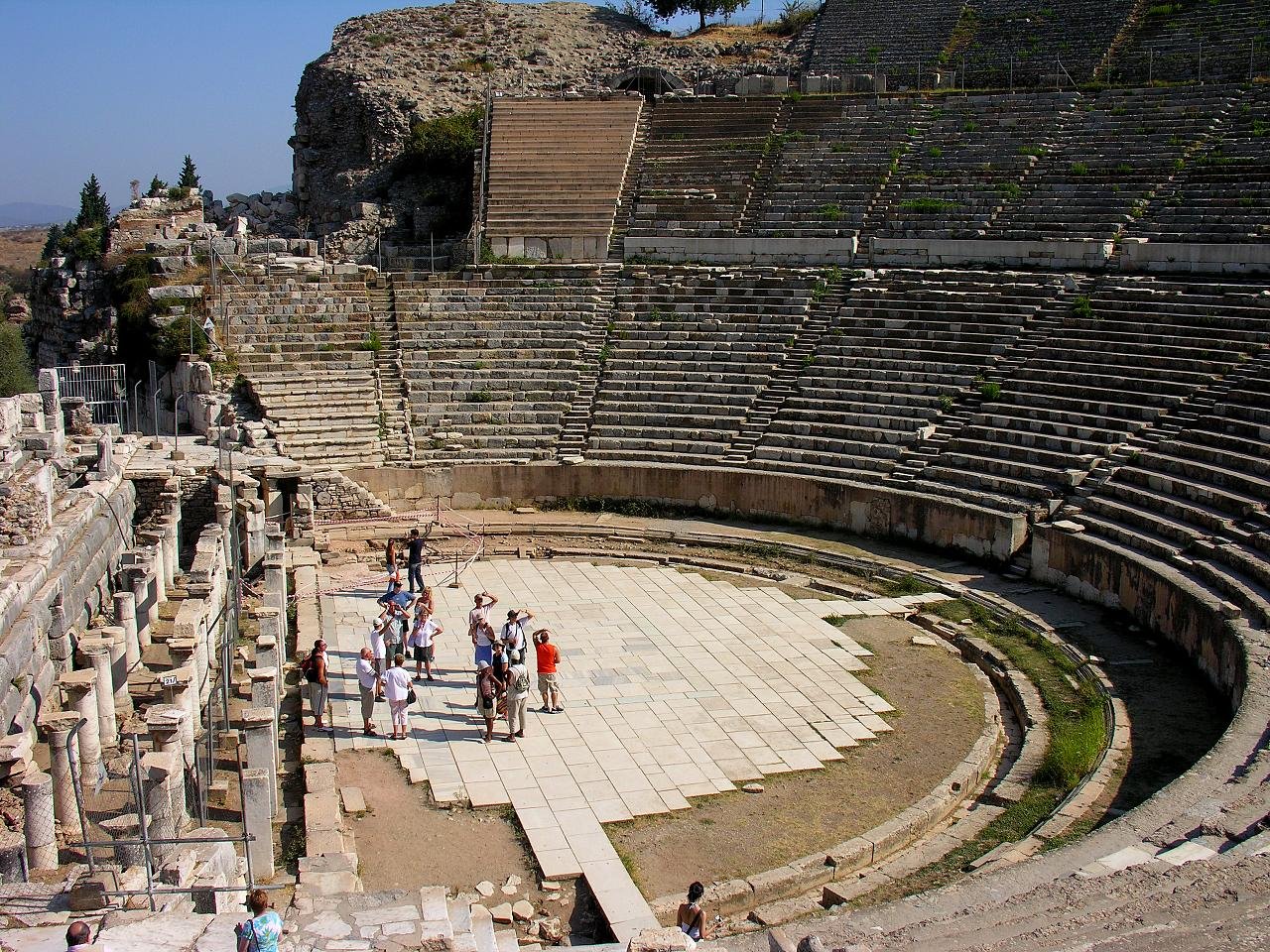 The tiered marble seating and orchestra of the Great Theatre of Ephesus, with visitors standing on the stage floor